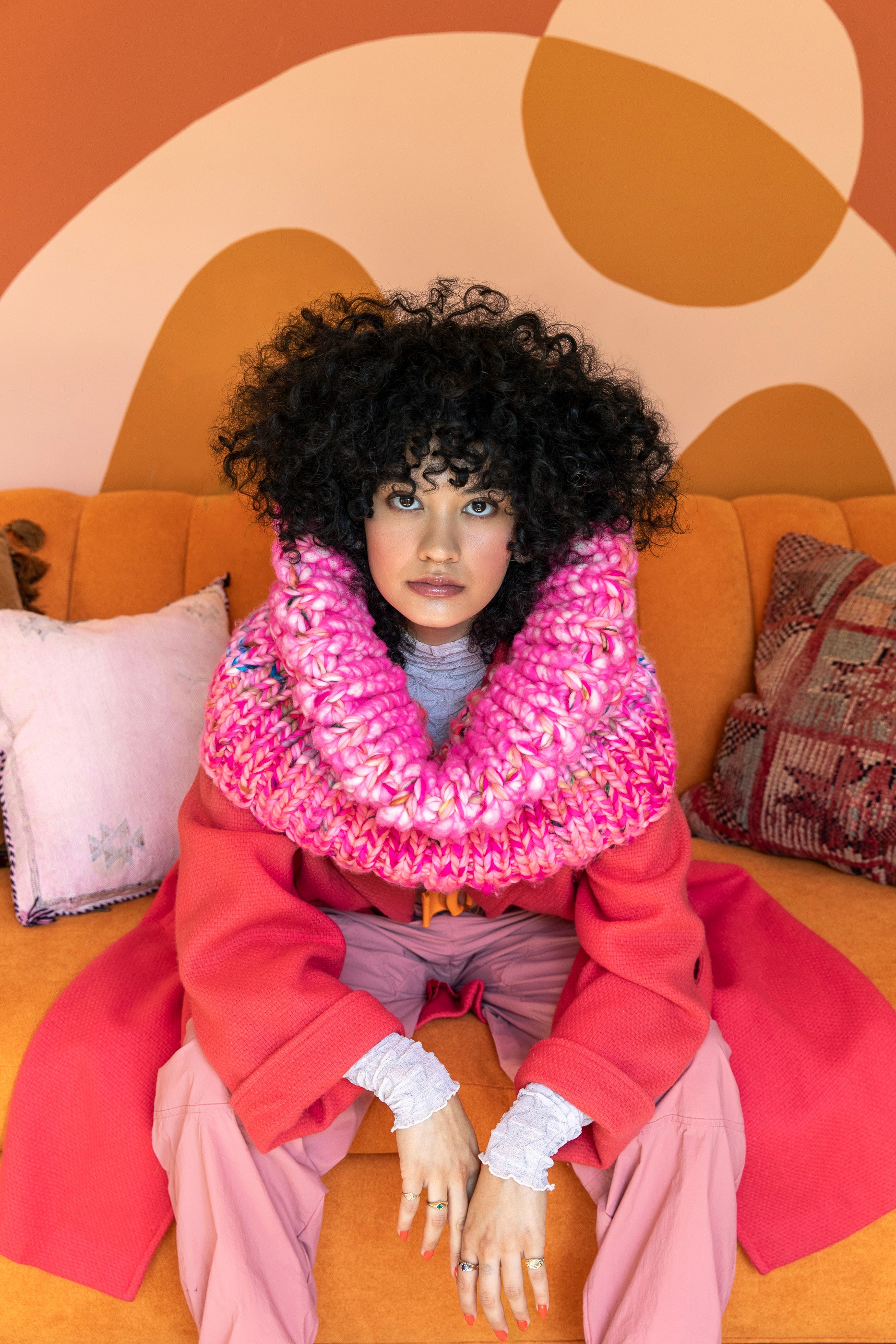 Silhouette of a person wearing a cap, viewed from behind, standing in front of a textured white canvas in a minimalist, dimly lit room.