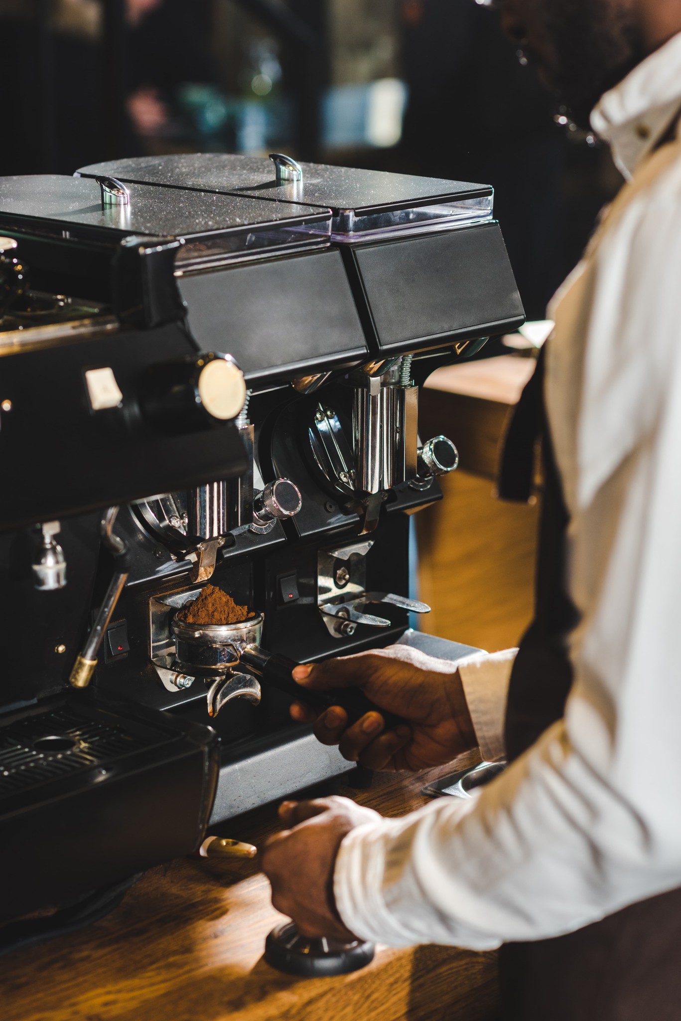 Barista preparing espresso at a professional coffee machine in a dimly lit café.
