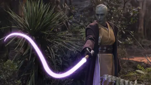 Vernestra Rwoh in gold robes holidng a purple lightsaber whip in the forest