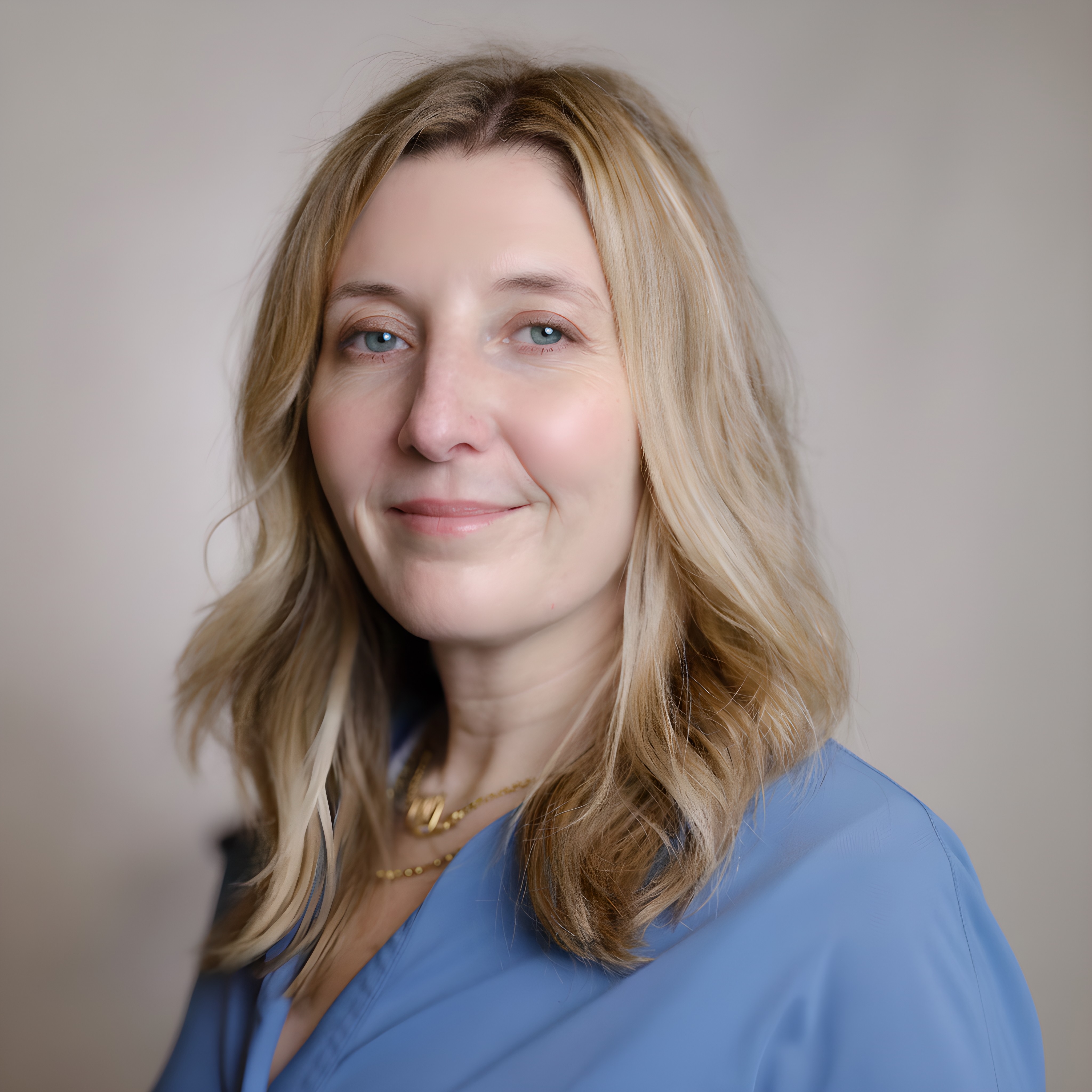 Close-up portrait of a smiling woman with long, light brown hair, surrounded by greenery in natural light.