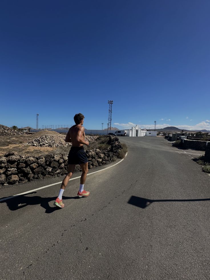 Determined woman walking on an outdoor running track, wearing a white cropped top with mesh sleeves and black track pants on a cloudy day.