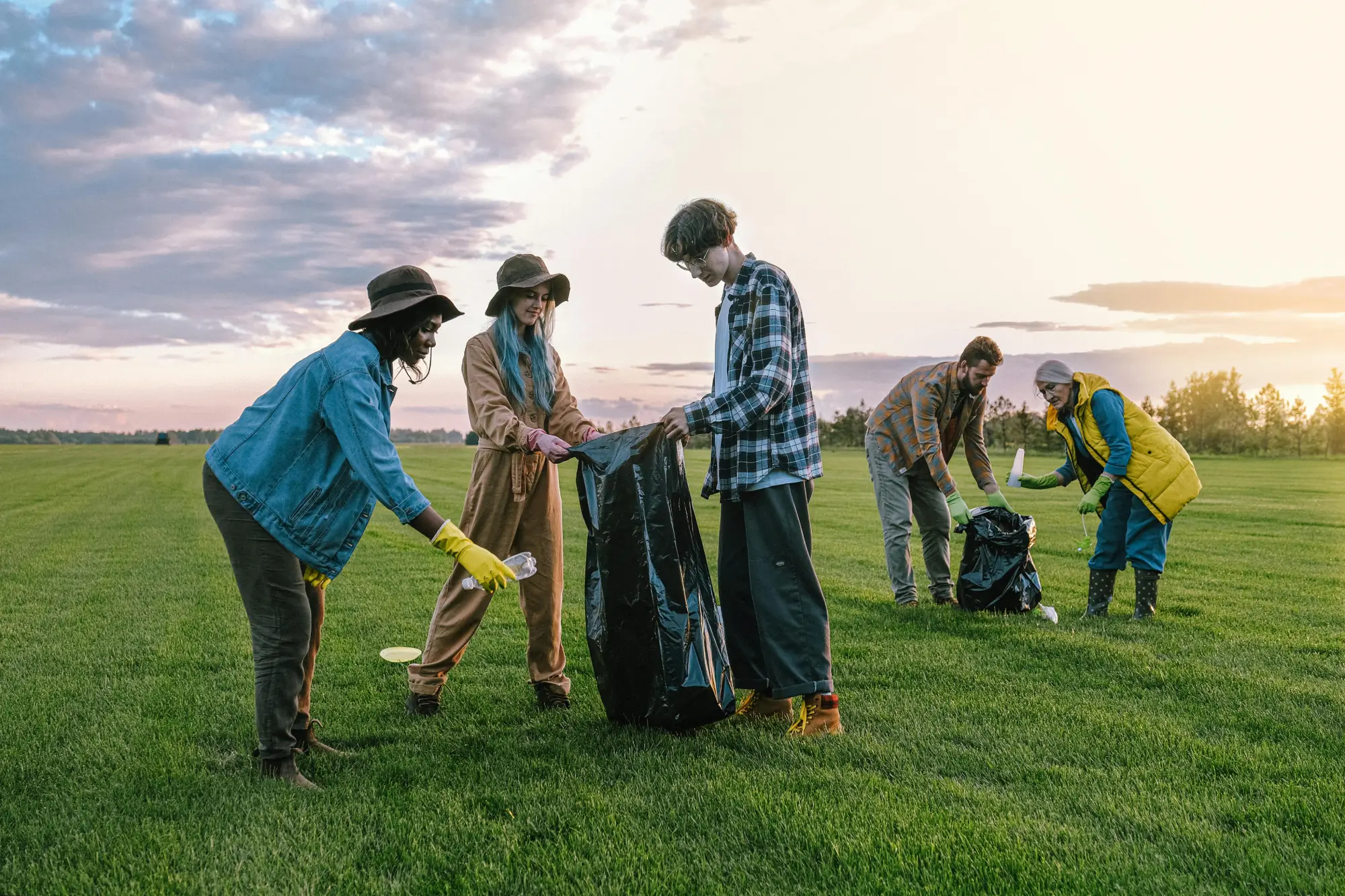 Group of people carrying out a clean-up activity in an open field at sunset.