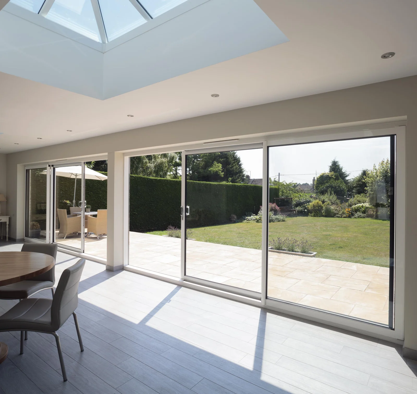 A garden room with an aluminium roof lantern above, a wide aluminium sliding door set and a bi-fold door, opening onto a lawn and patio