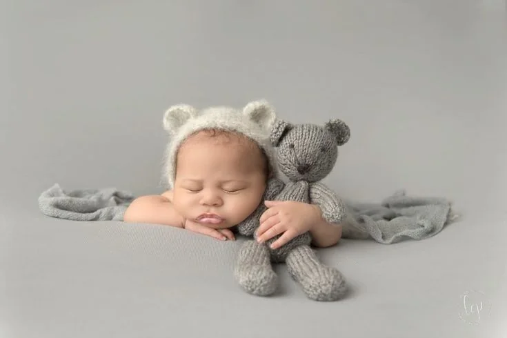 Sleeping baby in a bear bonnet holding a grey teddy
