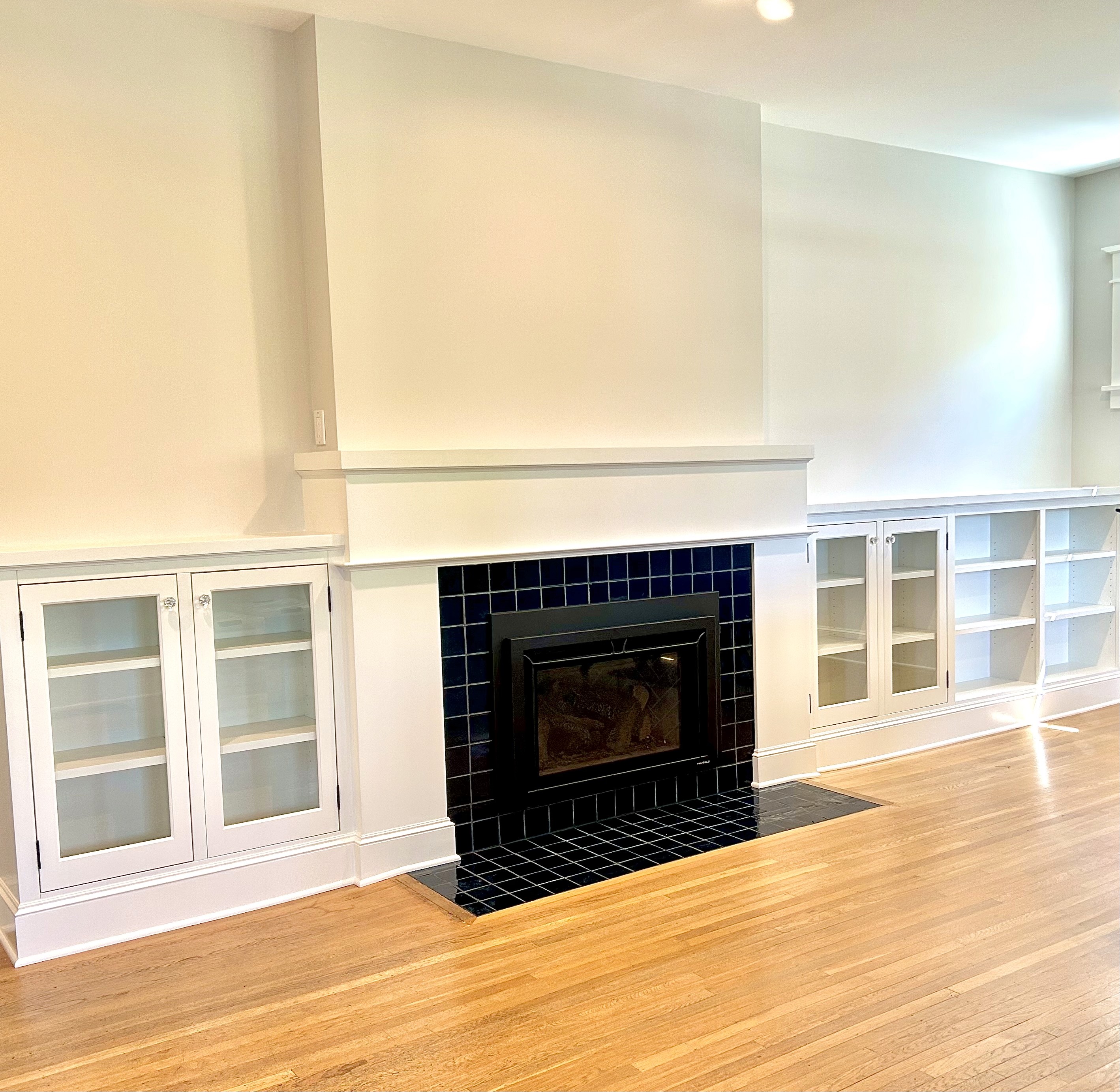 White and glass-fronted Shaker cabinets at chair rail height flank a fireplace with a dark tiled surround.