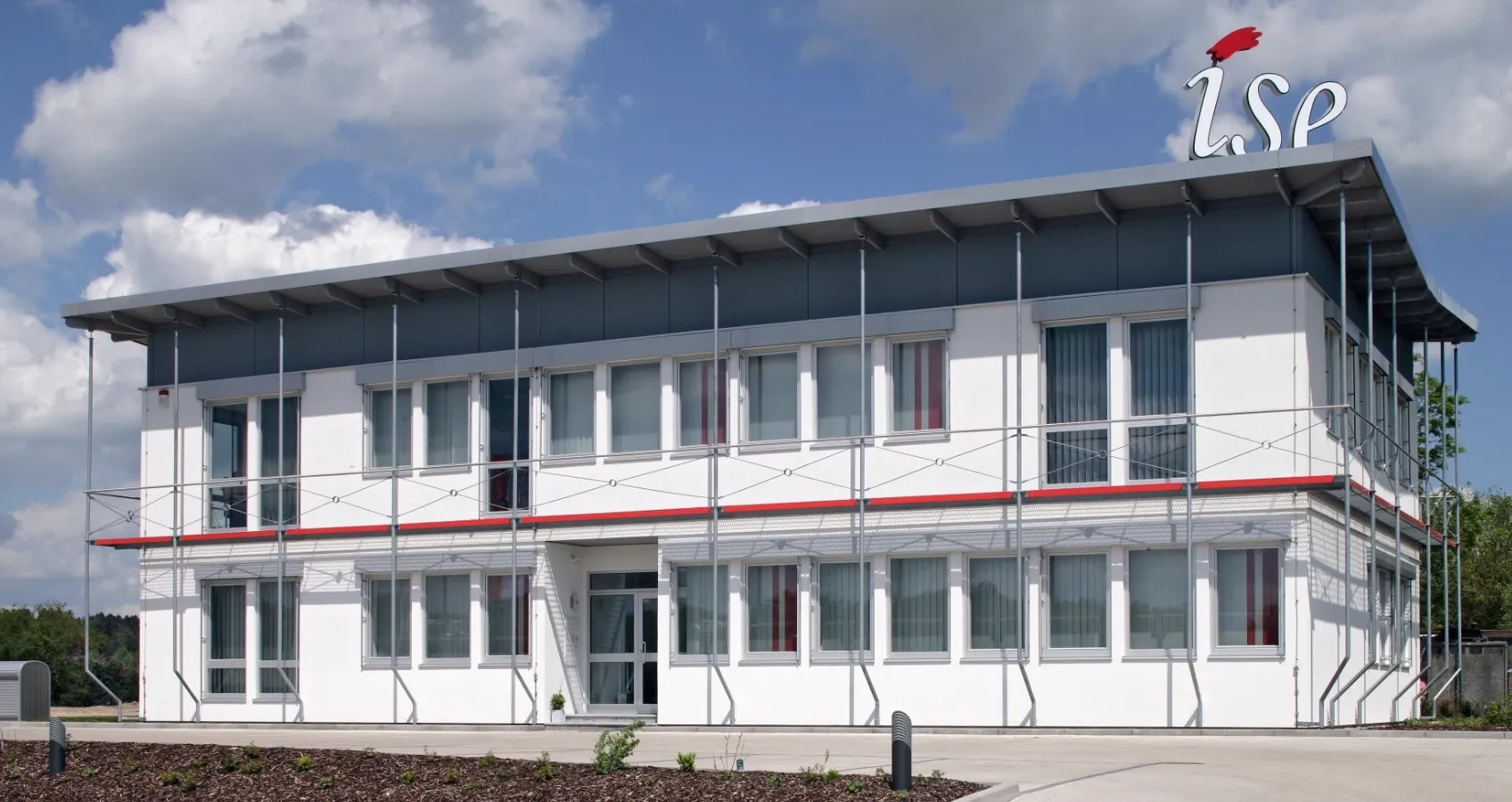 Modernes zweistöckiges Bürogebäude mit weißer Fassade, Fensterbändern und dem Schriftzug "ISE" auf dem Dach.