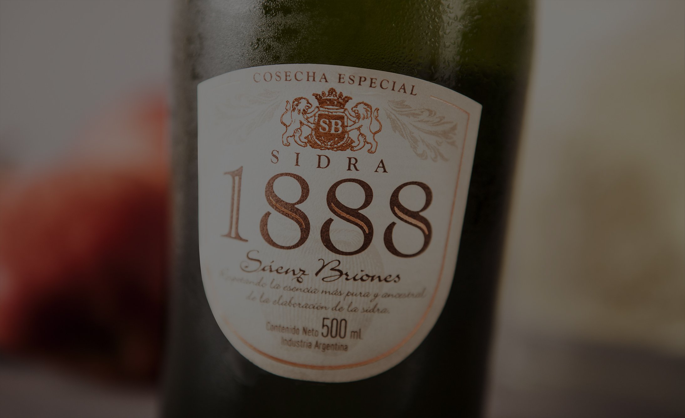 Close-up of a bottle of cider labeled '1888 Sidra' with an ornate emblem and text indicating it's a special harvest. Background is blurred.