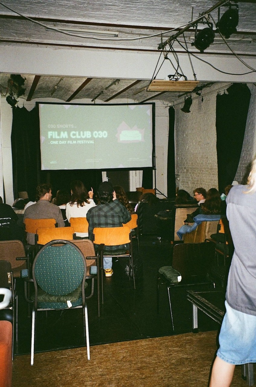 Ein voller Raum mit Zuschauenden die vor einer Beamerleinwand sitzen im Filmclub.