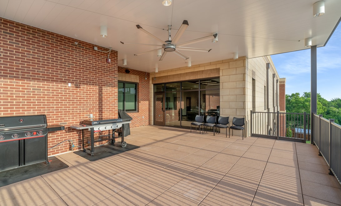 Covered patio with grills and ceiling fans against a brick wall at Mansfield Fire Station 1, by Martinez Architects