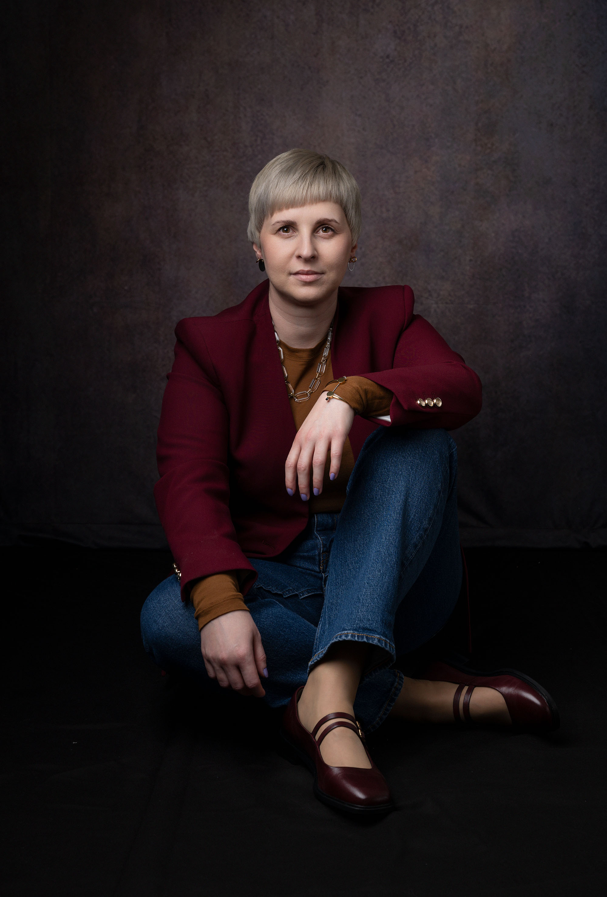 Founder portrait. Professional woman in blazer and jeans sitting cross-legged on the floor.