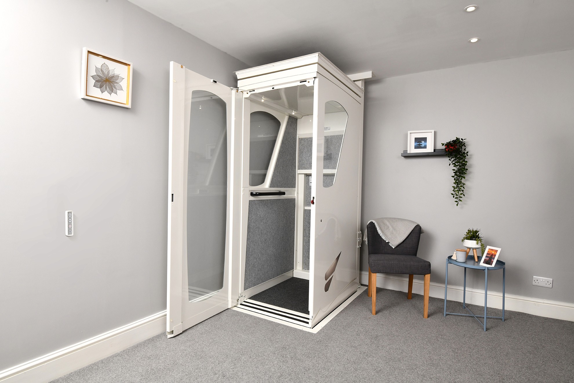 Elevate AVA home lift with door open installed in a residential room — white fully enclosed through-floor lift with glazed panels and grey carpeted interior