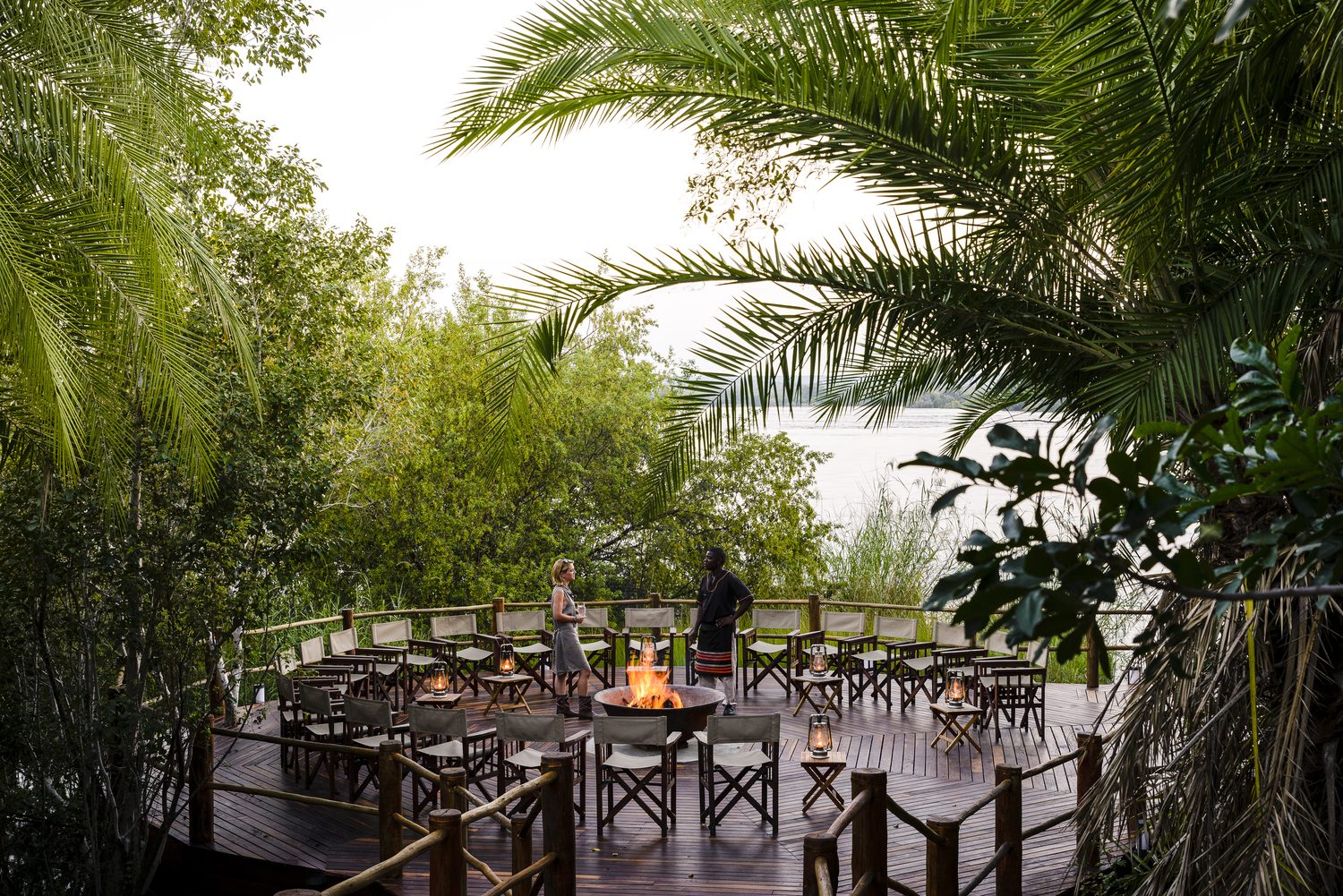 A firelit deck gathering beside the river at dusk