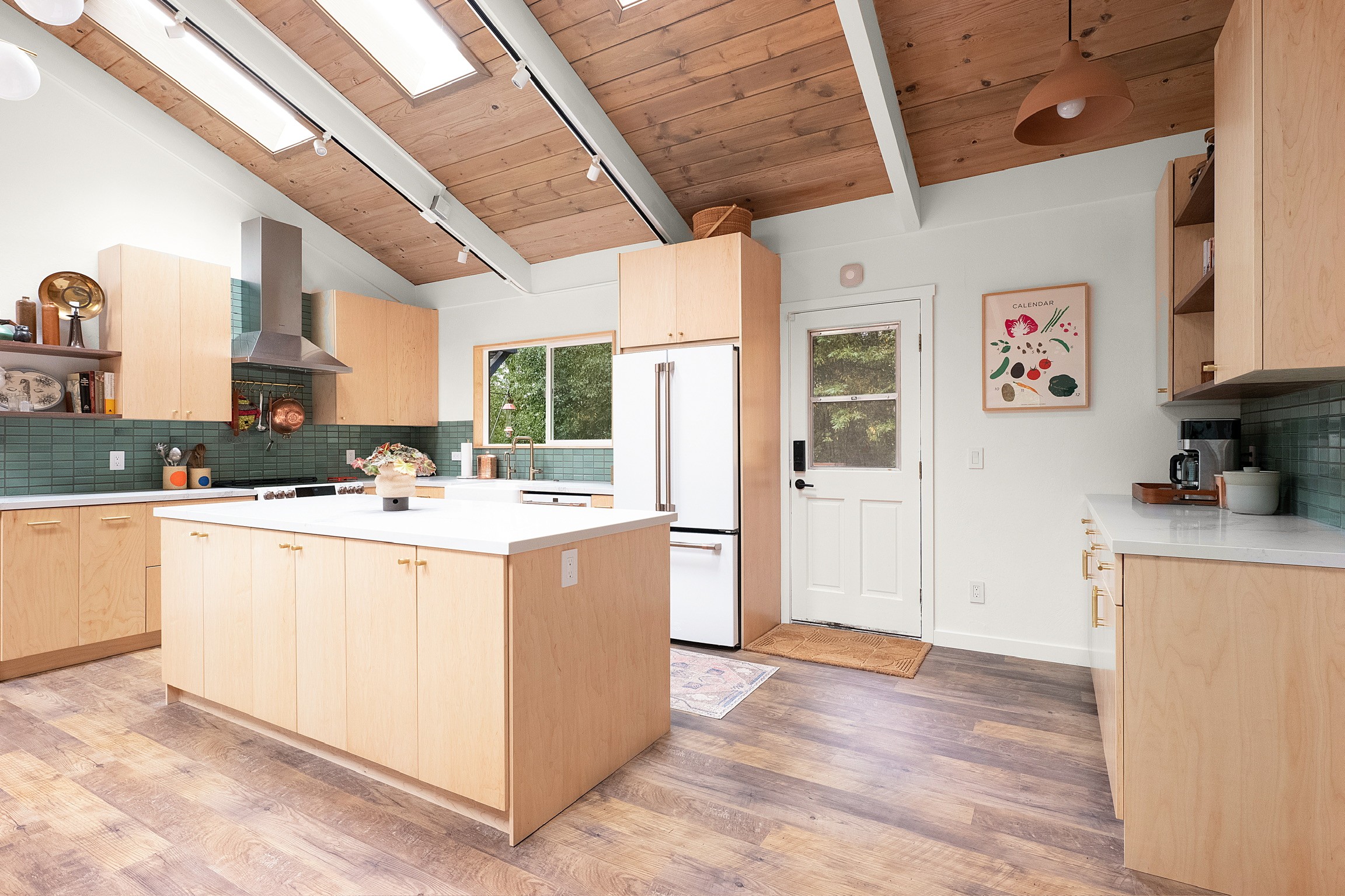 “Bright modern kitchen with light wood cabinets, large island, and wood ceiling with skylights”