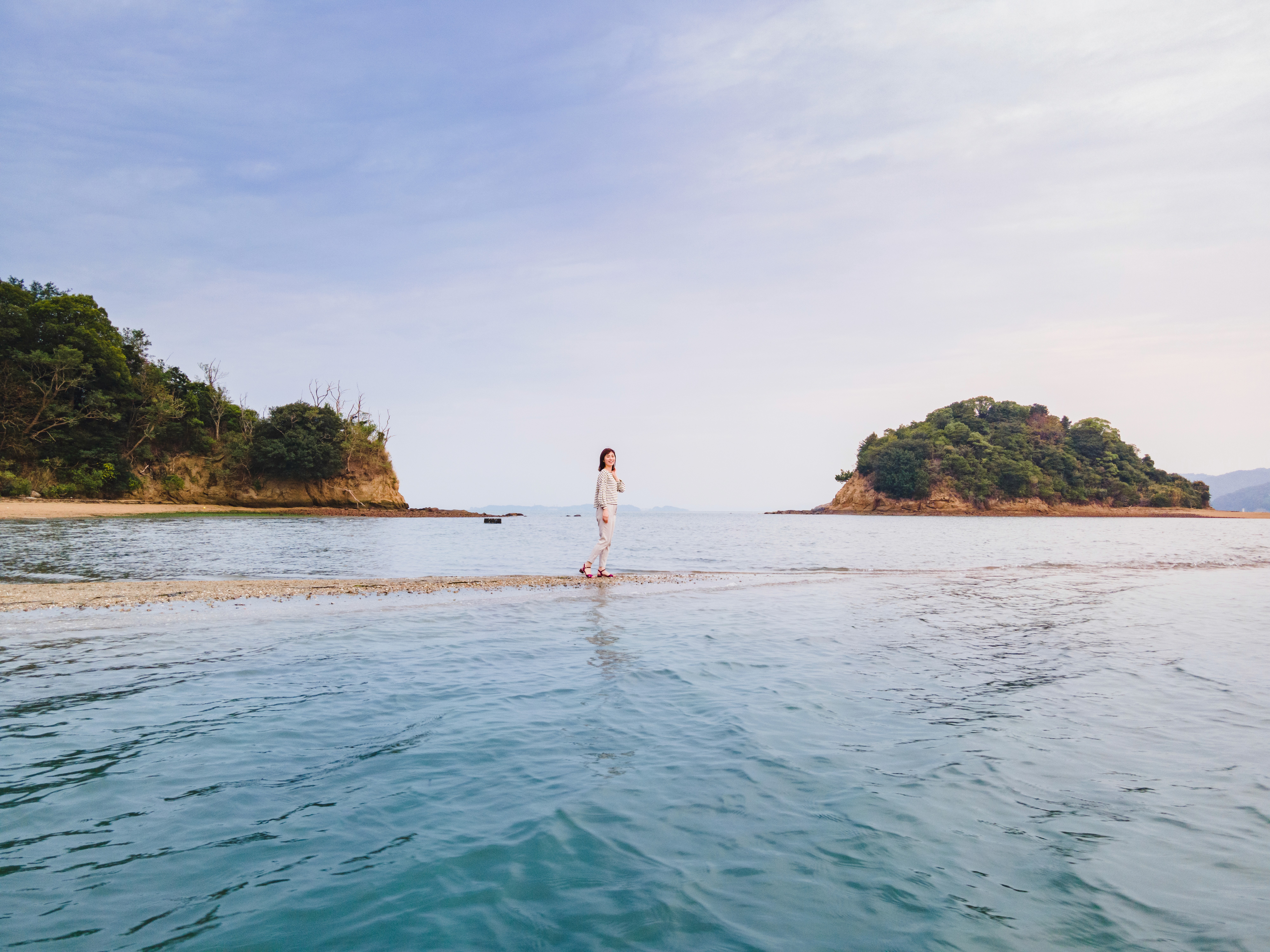 A woman walks along a sandy path that emerges from the Seto sea at low tide