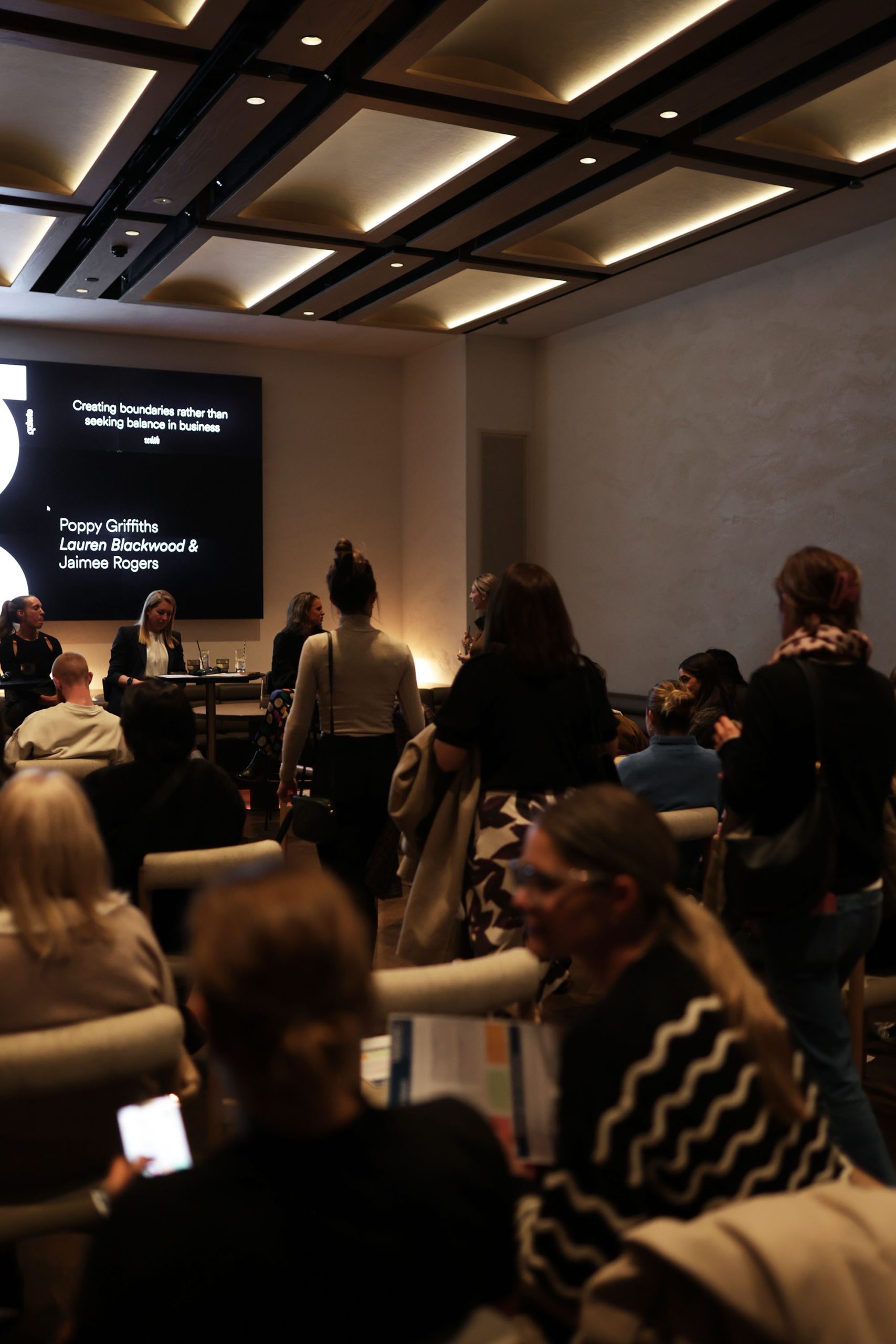 Screen reading Creating boundaries rather than seeking balance in business, with panellists Poppy Griffiths, Lauren Blackwood and Jaimee Rogers, audience seated and standing in the foreground