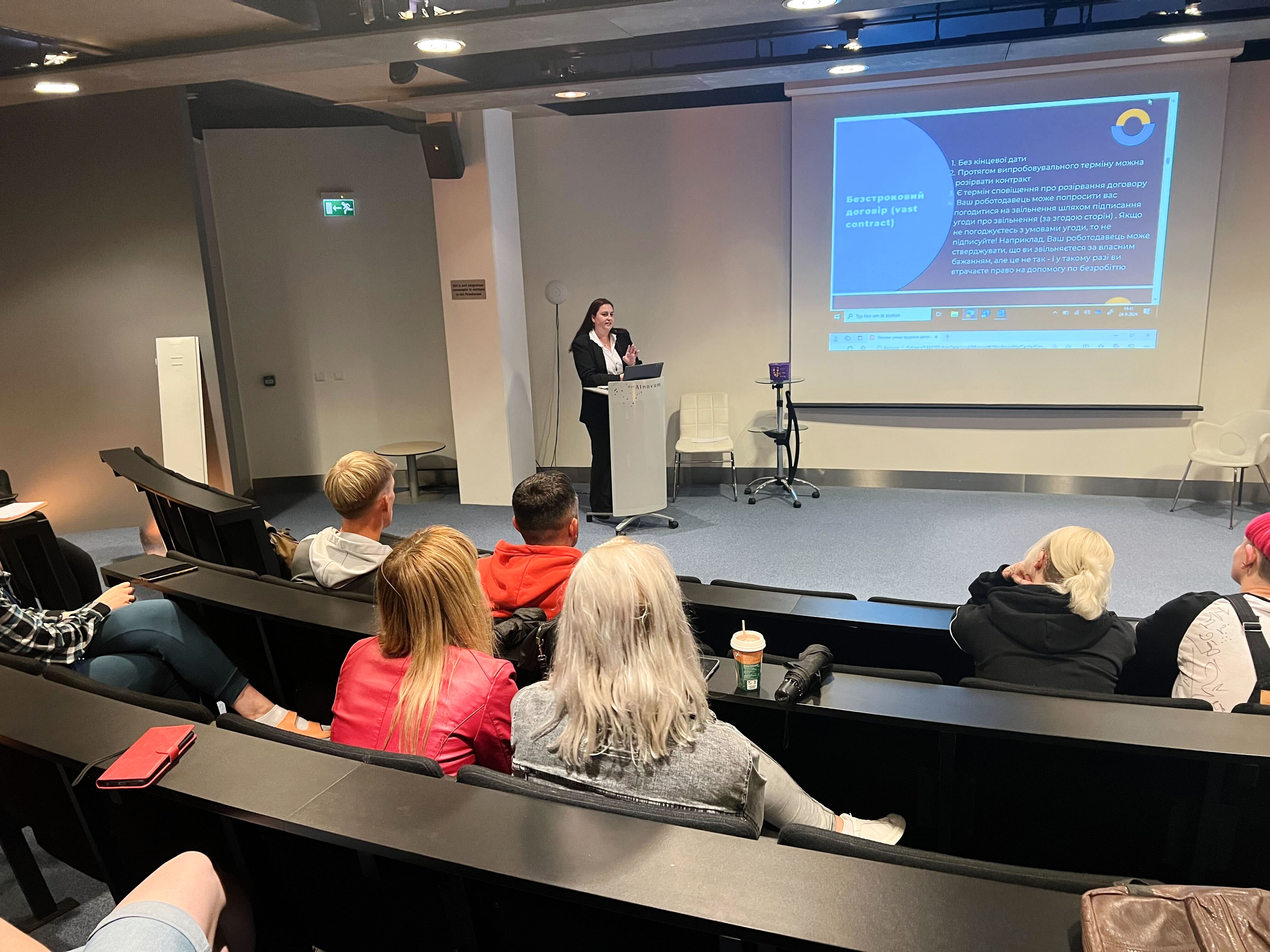 Presenter speaking to an audience during a session on Dutch labor law, with a presentation slide projected in the background.
