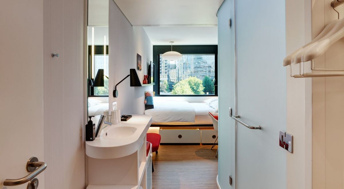 A cozy guestroom featuring a a solid surface vanity, closet niche and frosted glass shower pod in the foreground.