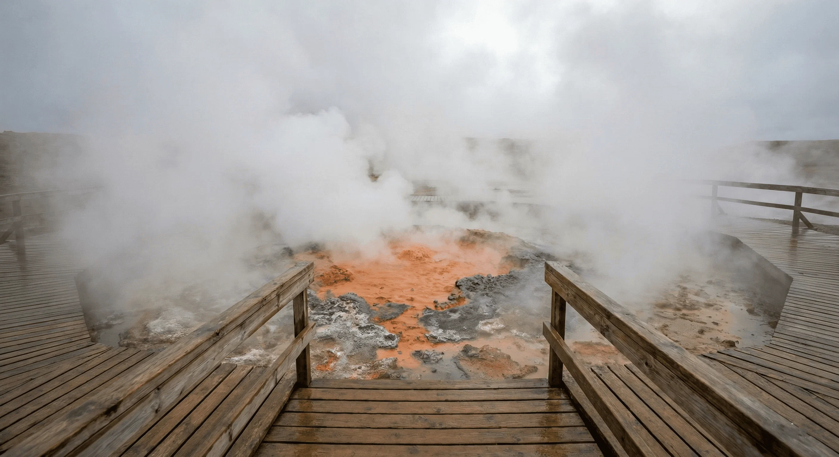 A wooden viewing platform overlooking a steaming geothermal vent with colorful orange and grey mud.