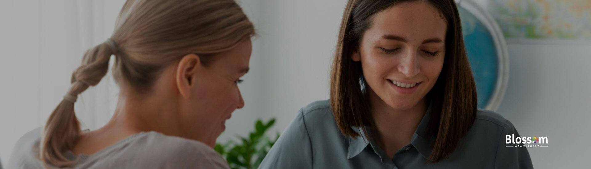 Two women sit at a table, smiling and looking at an FBA with one pointing at the paper.