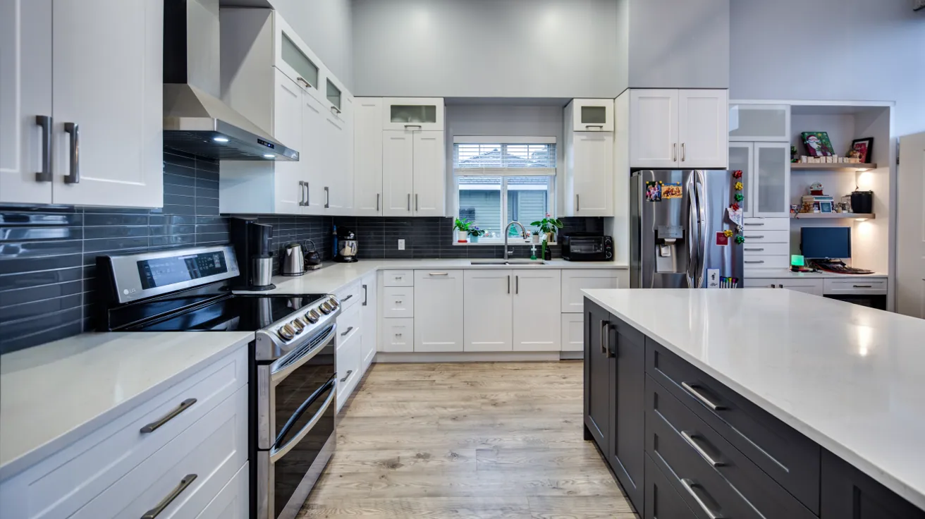 Modern L-shaped kitchen in custom Vancouver home featuring two-tone cabinetry with white uppers and gray lowers, horizontal black tile backsplash, quartz countertops, and efficient work triangle layout