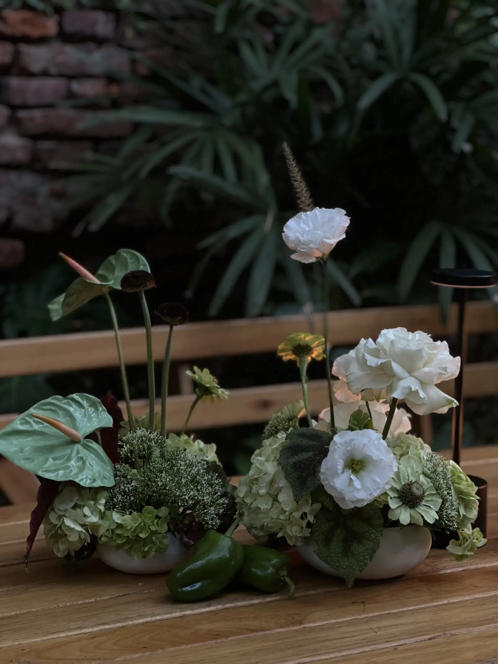 Centros de mesa con flores blancas y verdes sobre mesa de madera, ambientación natural con hojas tropicales.