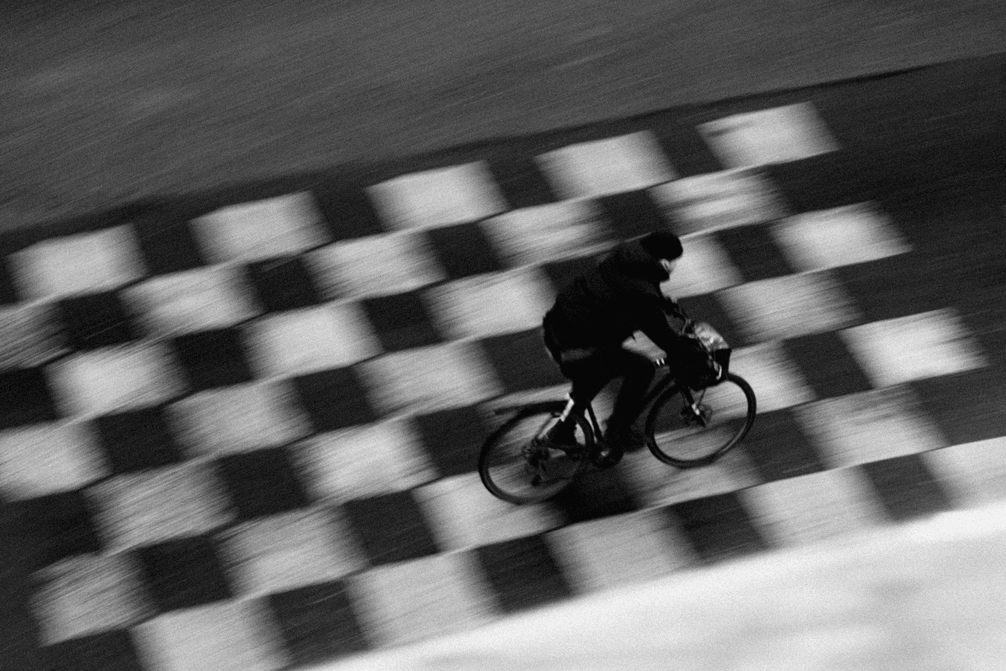 Black-and-white image of a cyclist in motion, captured with motion blur against a patterned track