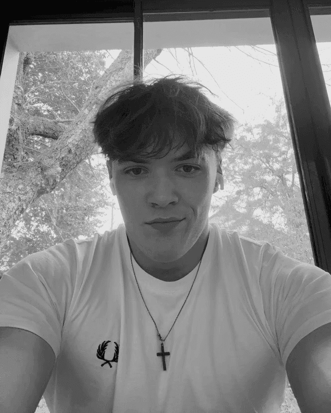 Portrait of a young man with short hair, wearing a dark t-shirt, against a plain background.