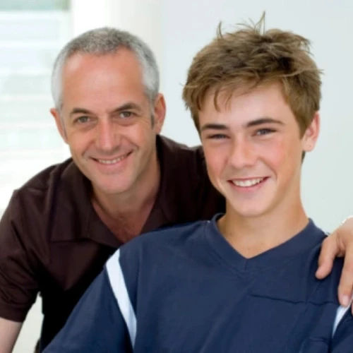 Smiling father and teenage son posing together inside a clinic consulting room in Coburg, Melbourne.