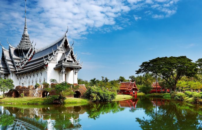 Vineyard rows under leafy foreground frame a Tuscan villa on a misty hill