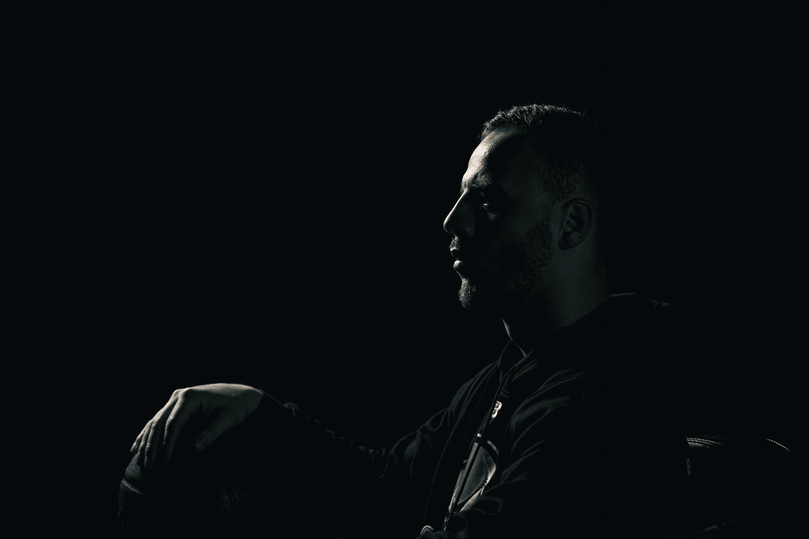 Portrait en clair-obscur d’un homme de profil dans un environnement sombre.