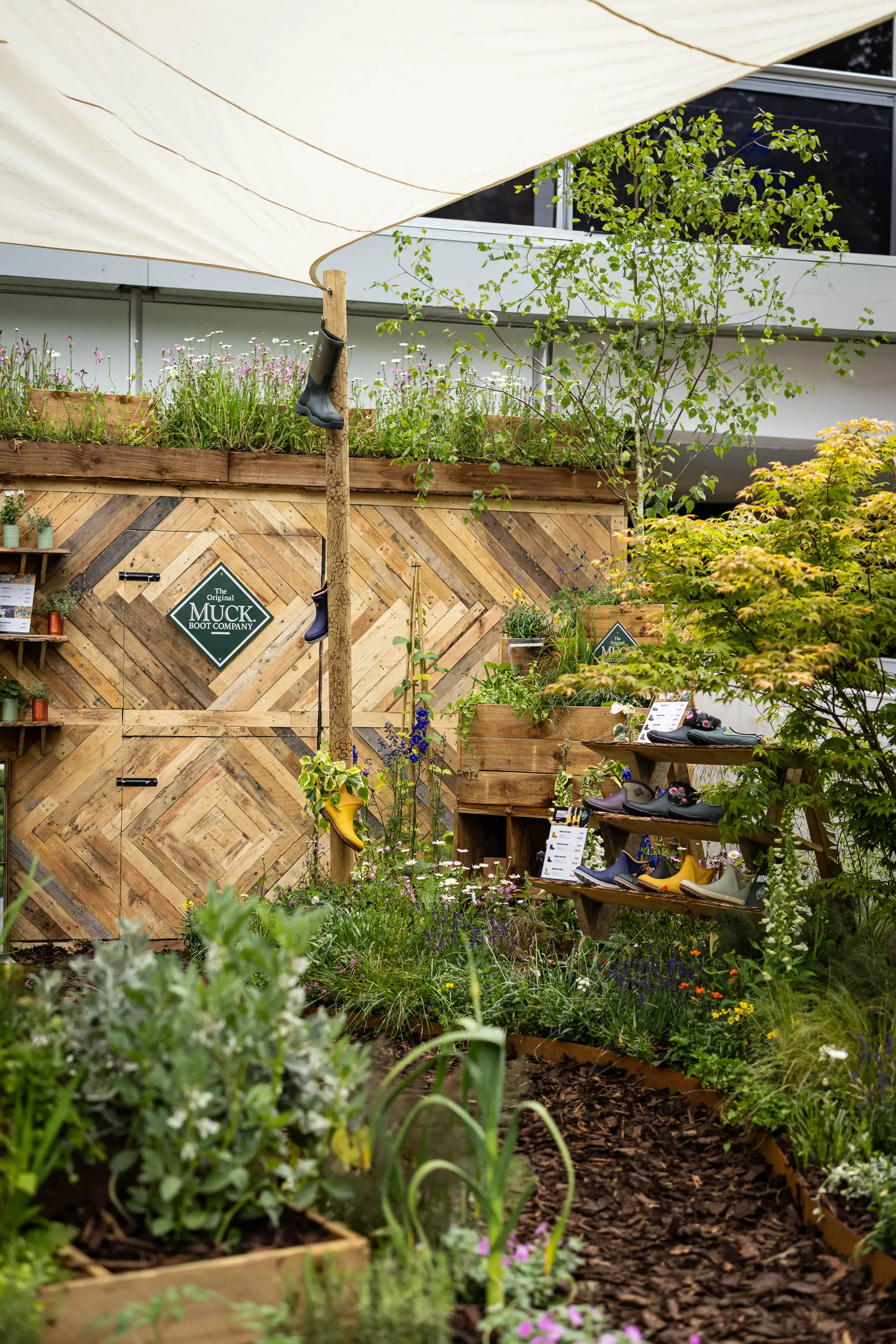 A lush garden with various plants, featuring a brick wall and greenery, under a roof overhang.