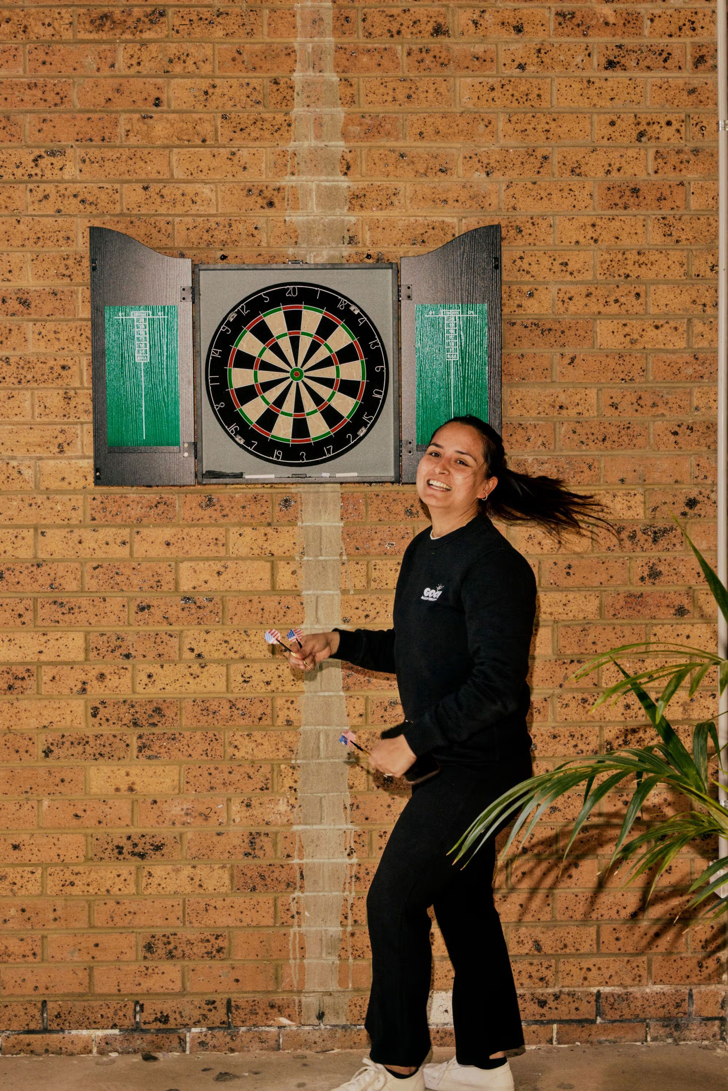 Team member smiling and playing darts in the Good Maintenance workshop.