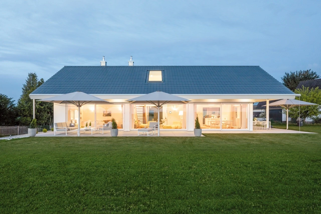 Modern house with large windows, patio, and lawn at dusk.