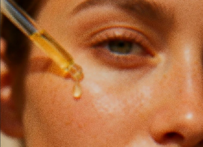 Face serum dropper applied to glowing skin closeup