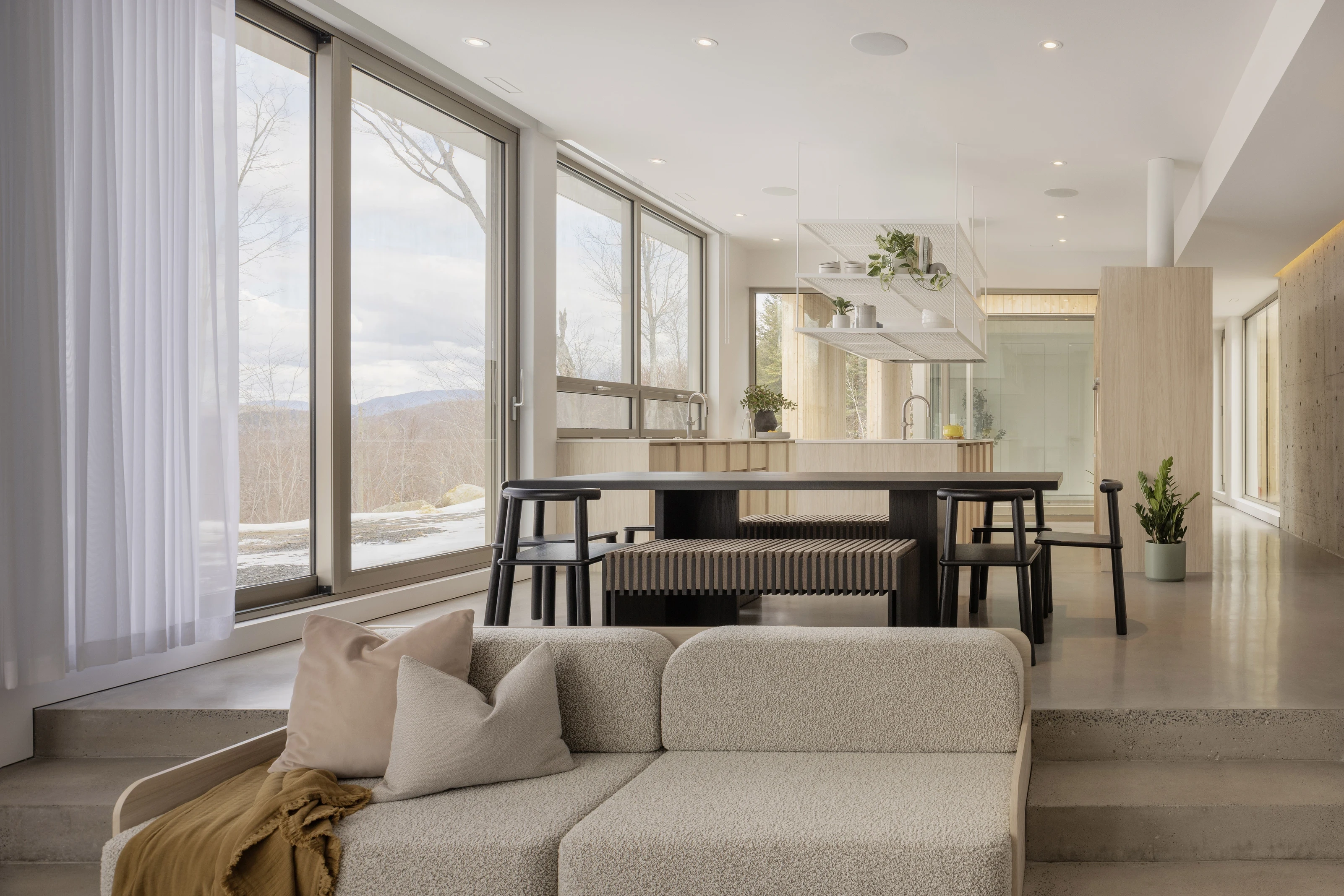 A modern living space featuring large windows, a light-colored sofa, and a dining table with minimalist decor.