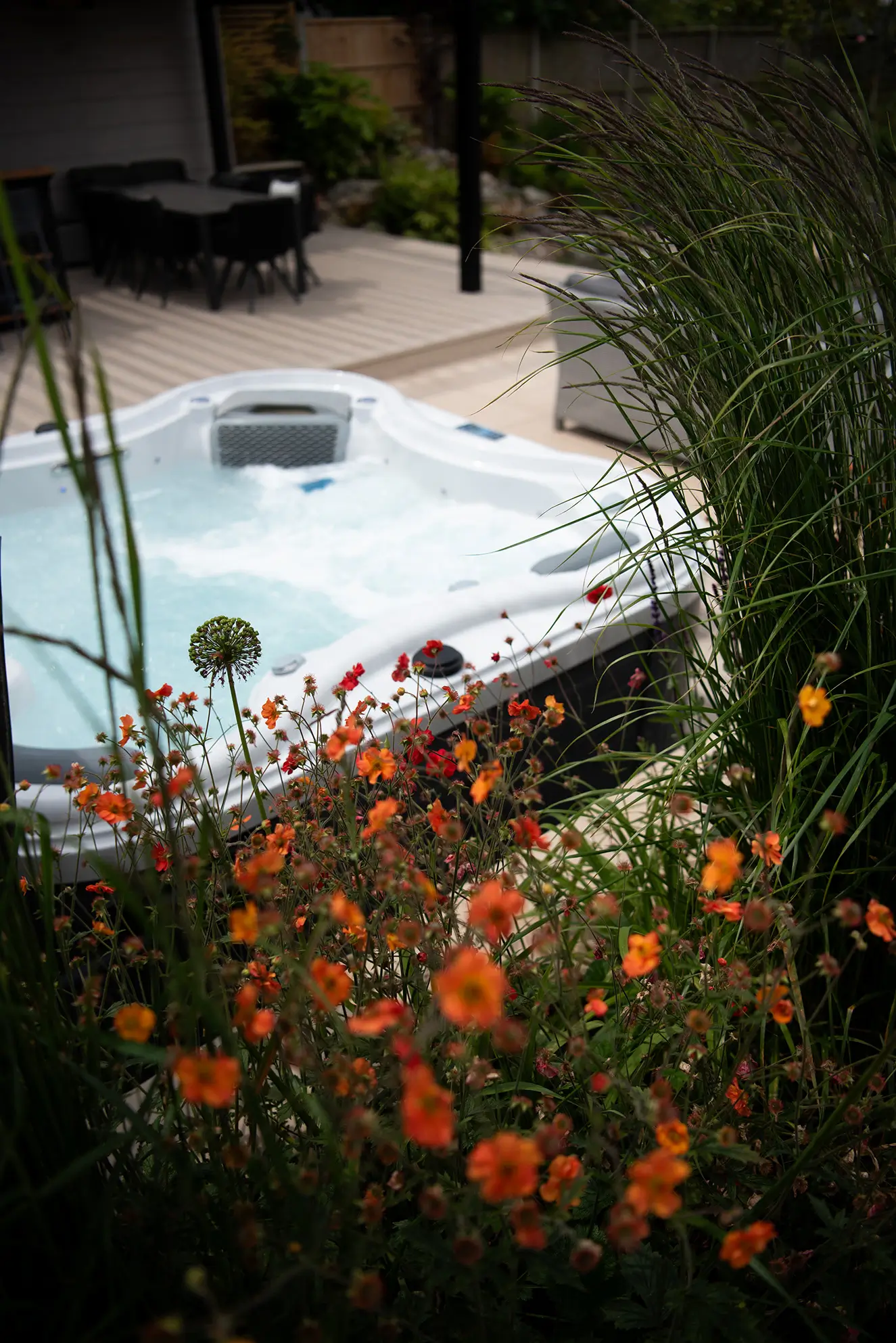 A tranquil garden scene featuring a hot tub surrounded by vibrant orange flowers and greenery.