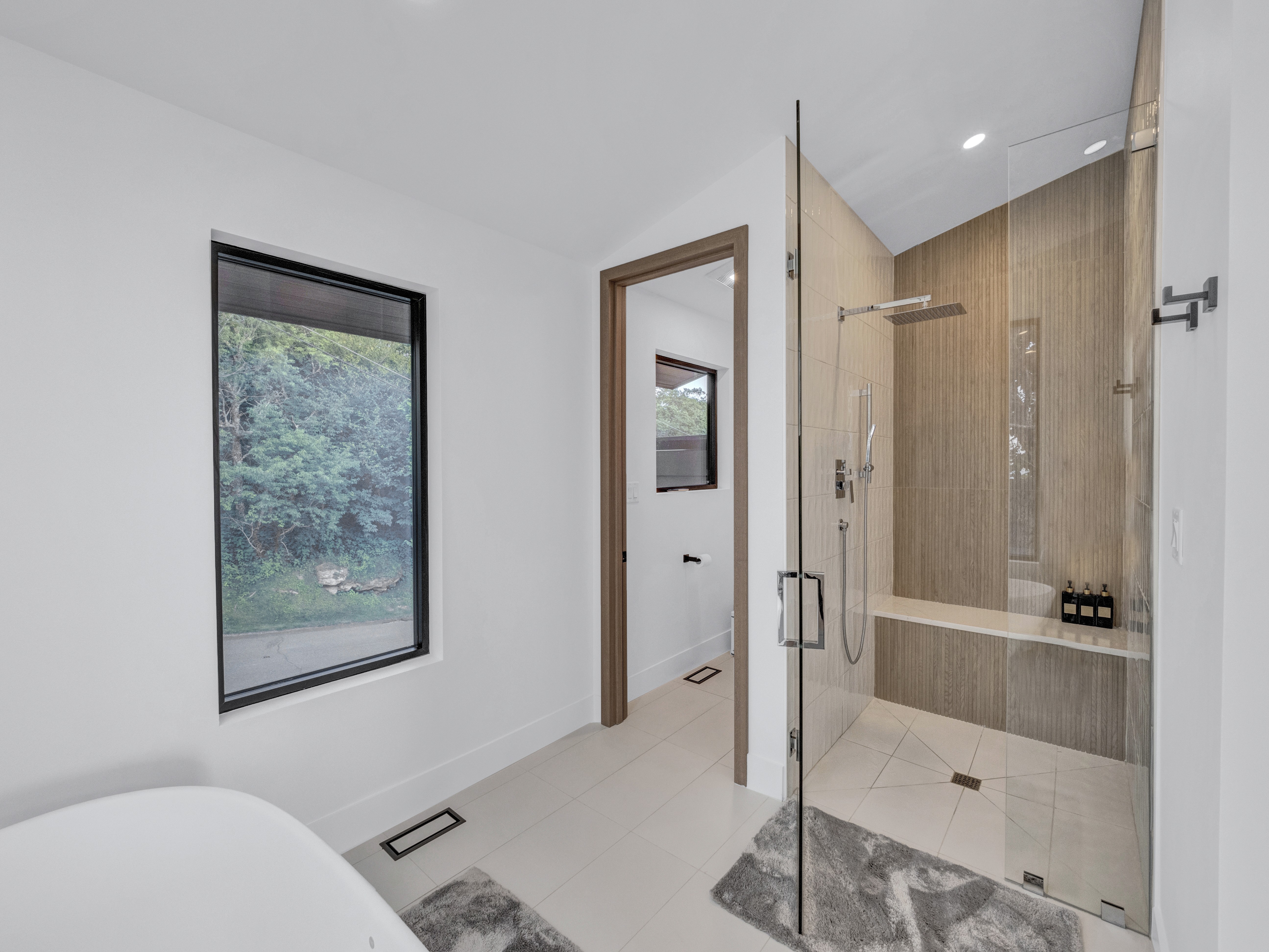 Wide view of the master ensuite showing the glass shower, soaking tub, and forest-view window