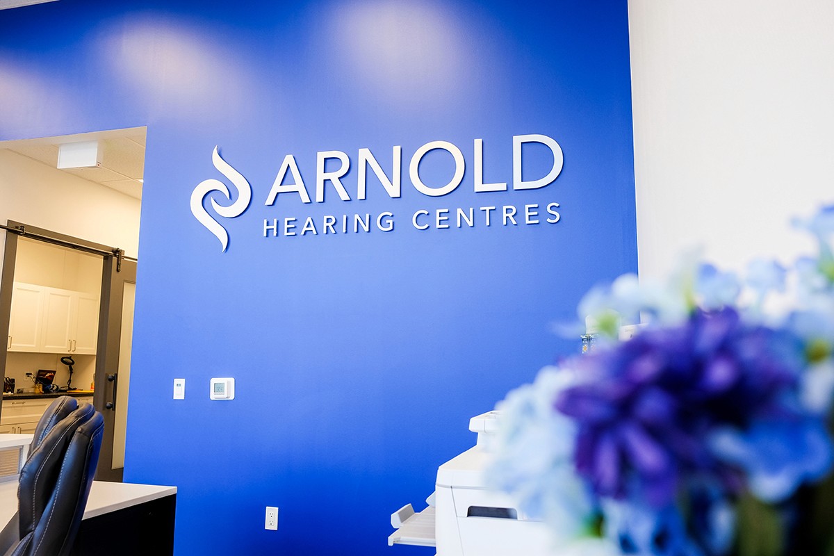 Interior of an office with a blue wall displaying the "ARNOLD" logo and a blurred bouquet of blue flowers in the foreground.