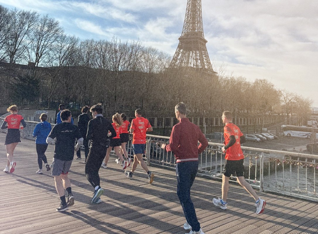 Des participants courent ensemble lors d'un événement sportif sur un pont parisien, avec la Tour Eiffel en arrière-plan, créant une scène dynamique d'une course en plein air.