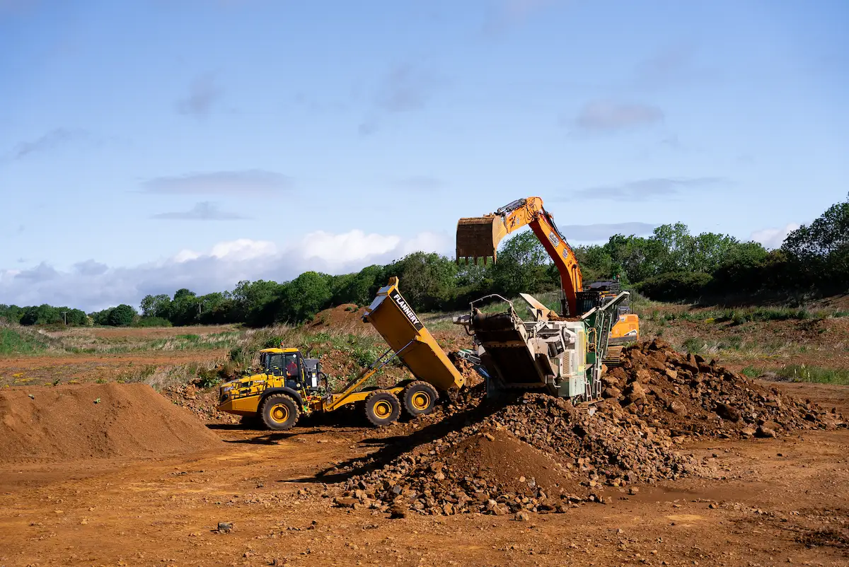 Excavator and dump truck operating under site contracting supervision during bulk material processing on a commercial infrastructure project.