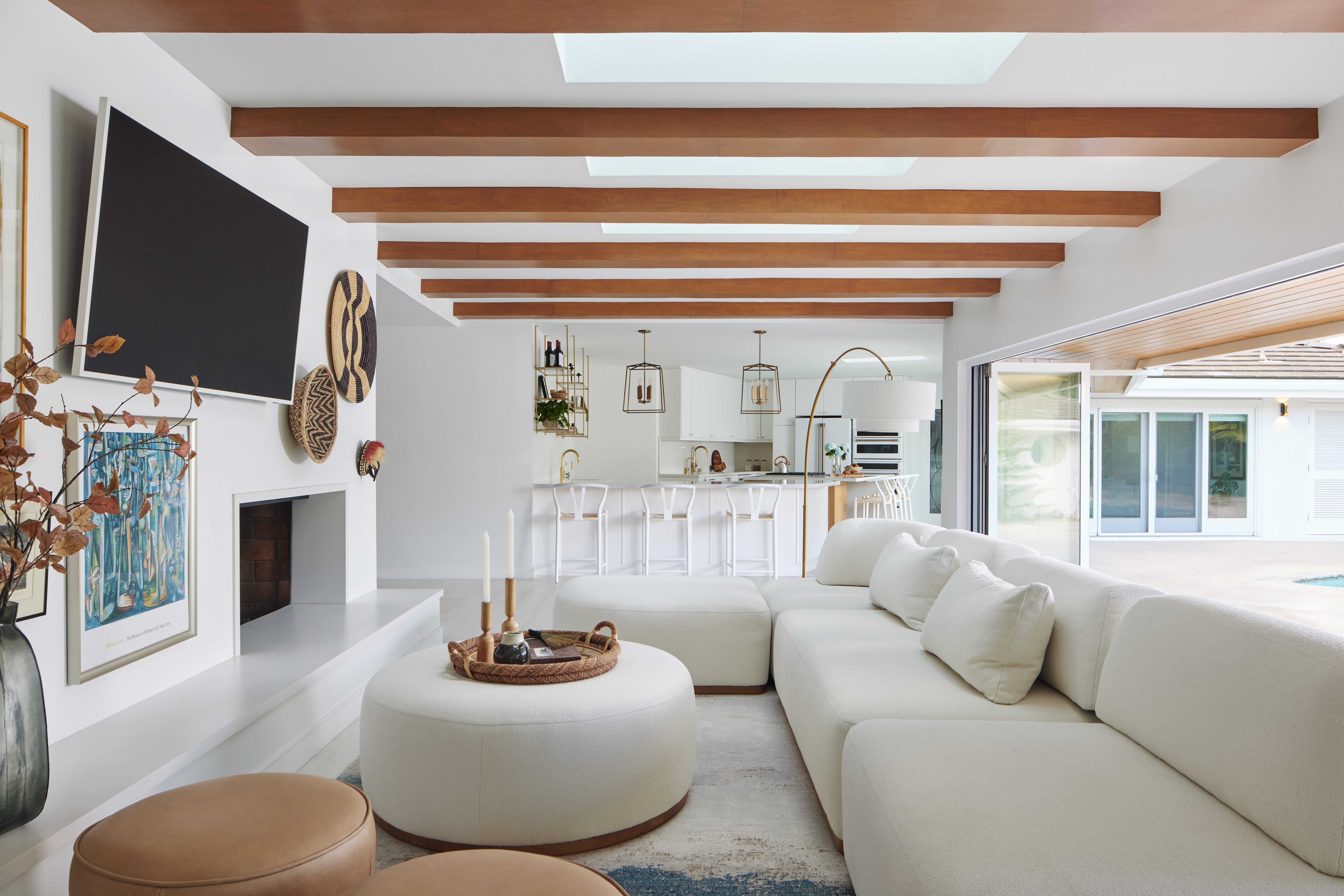 Open concept and airy family room and kitchen with exposed wood beams, boucle modular sofa, and bi-fold doors that open to the backyard by Jubilee Interiors in Los Angeles, California