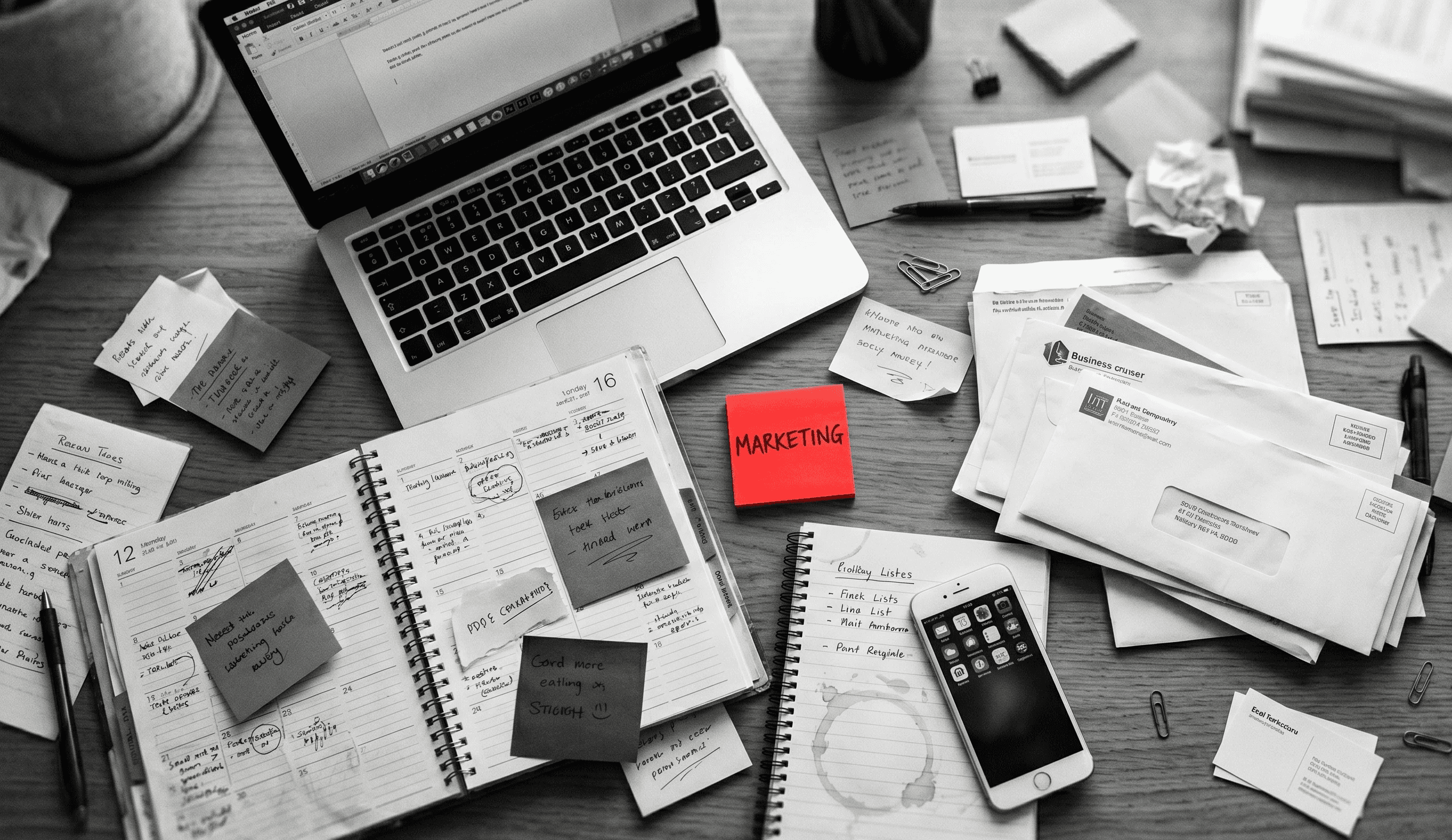 Overhead view of a cluttered small business owner's desk with a red sticky note labeled marketing, illustrating how marketing tasks get buried