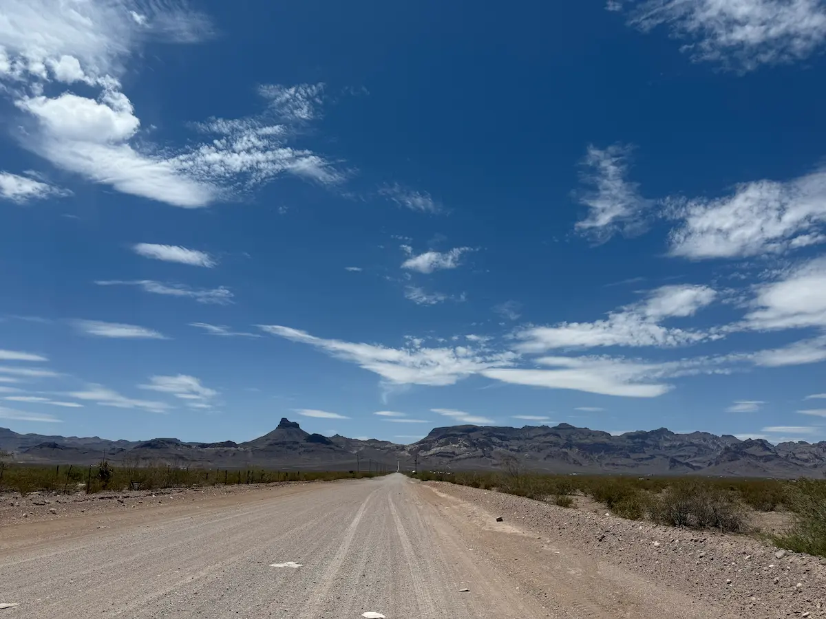 A long dirt road stretching through the desert with distant mountains under an open sky in Arizona.