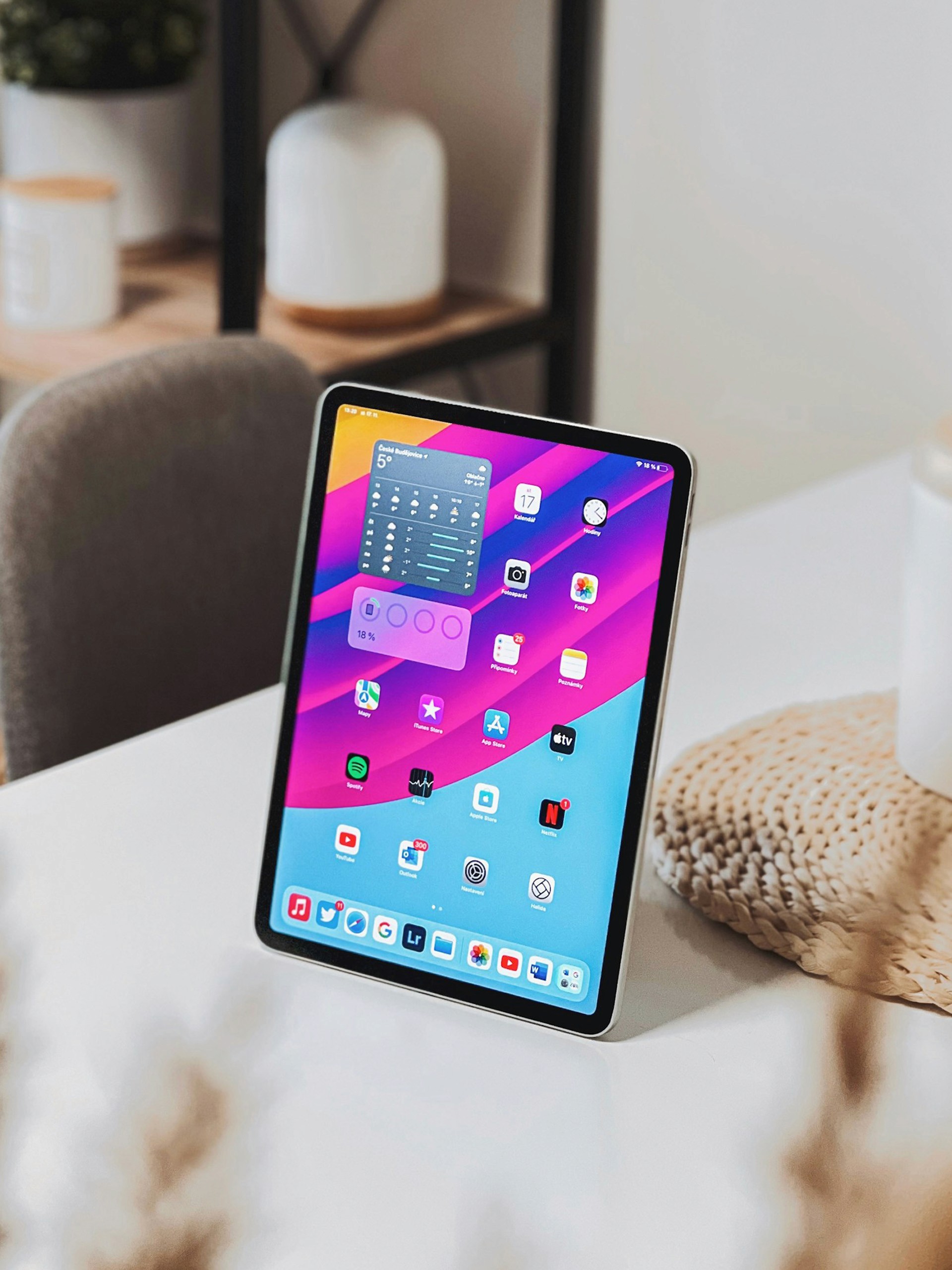 A tablet on a white table displaying a colorful home screen with apps and widgets in a bright room.
