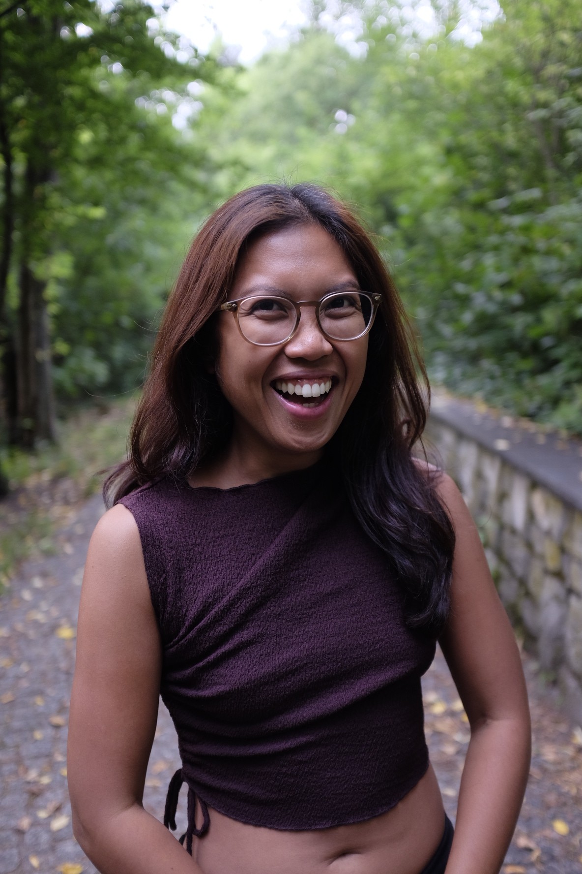 Una persona con una camiseta negra y pantalones de color claro está de pie en la cima rocosa de una montaña al atardecer, sosteniendo una cámara frente a su cara para tomar una foto. Un mar de nubes se extiende detrás de ellos, iluminado por la luz dorada del sol poniente.