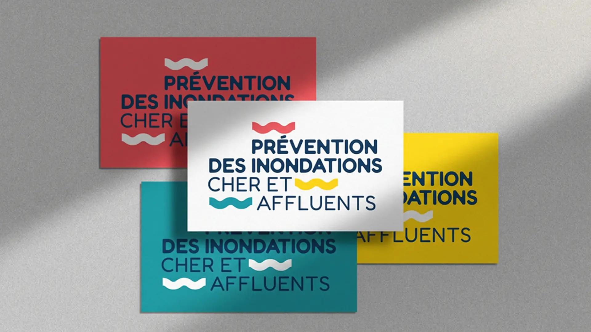 Mise en situation de l'identité visuelle 'Prévention des inondations Cher et affluents' sur des cartes de visite déclinées en quatre coloris avec un jeu d'ombres portées.