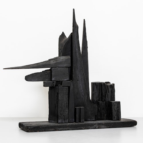 Scultura astratta nera con forme angolari e geometriche disposte su una base piatta contro uno sfondo bianco.