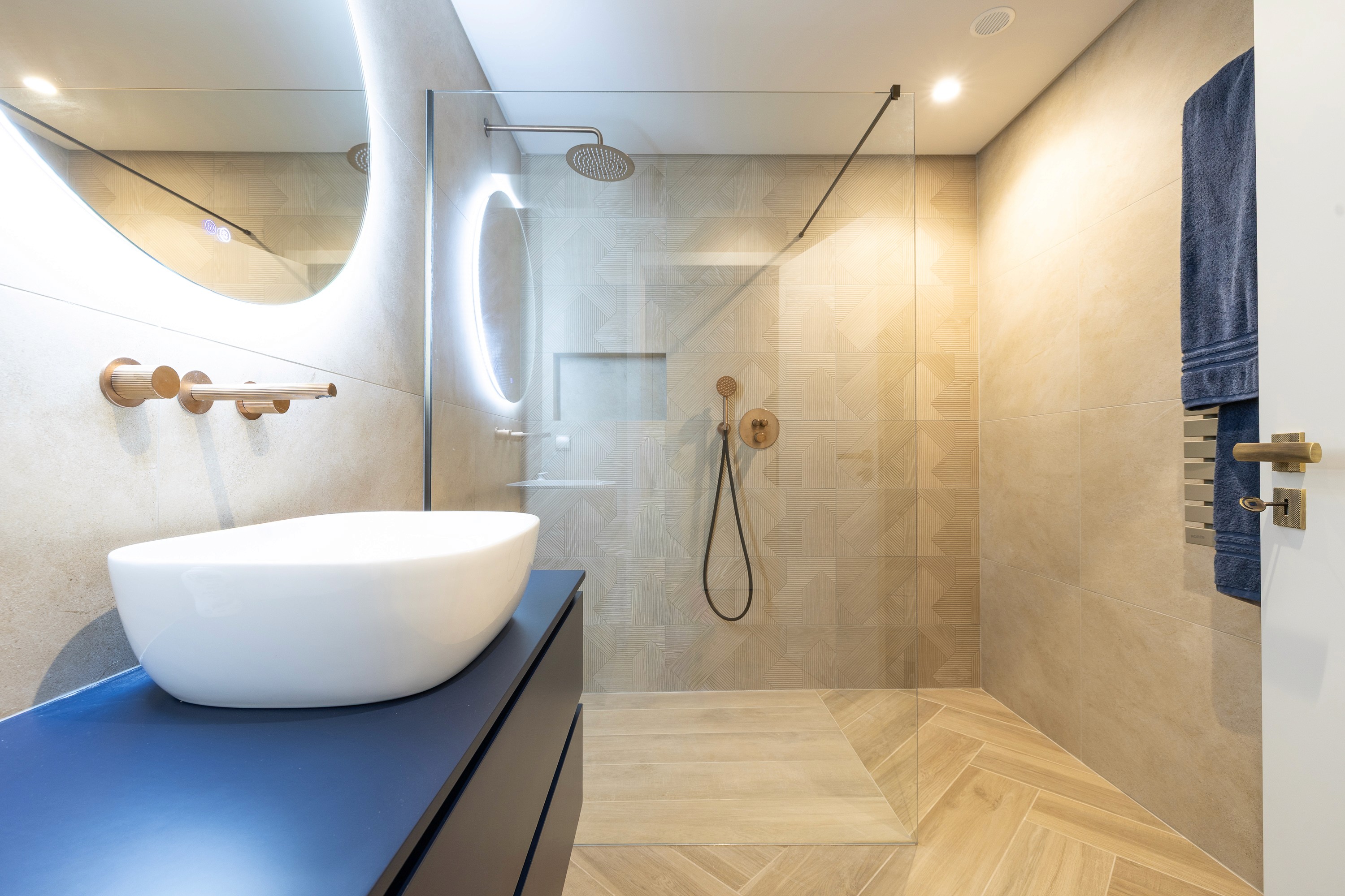 Main bathroom with a curved wall, a backlit oval mirror, a blue vanity and a walk in shower
