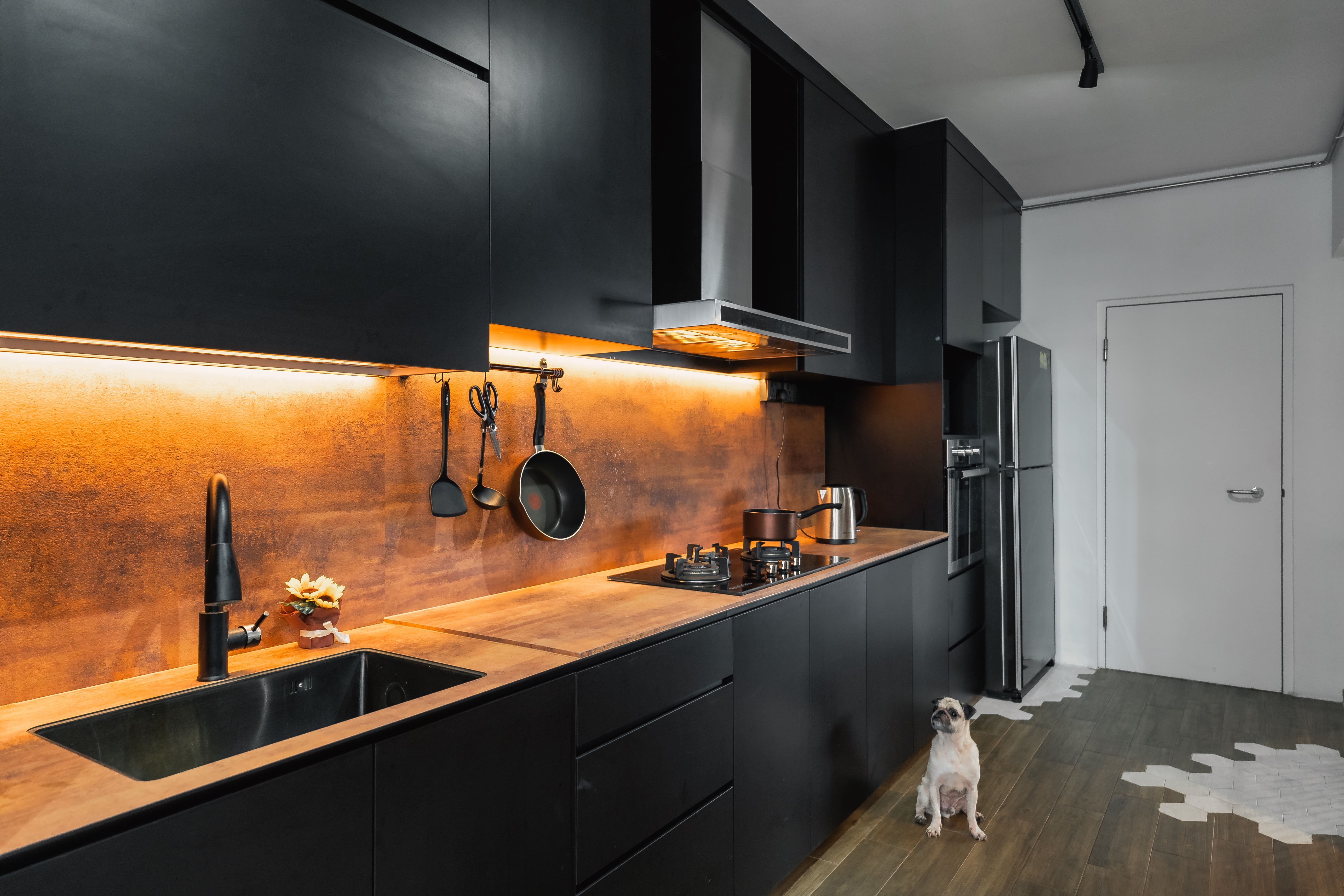 A full-length kitchen layout with striking black cabinetry and warm tones, accented by clever lighting and open storage
