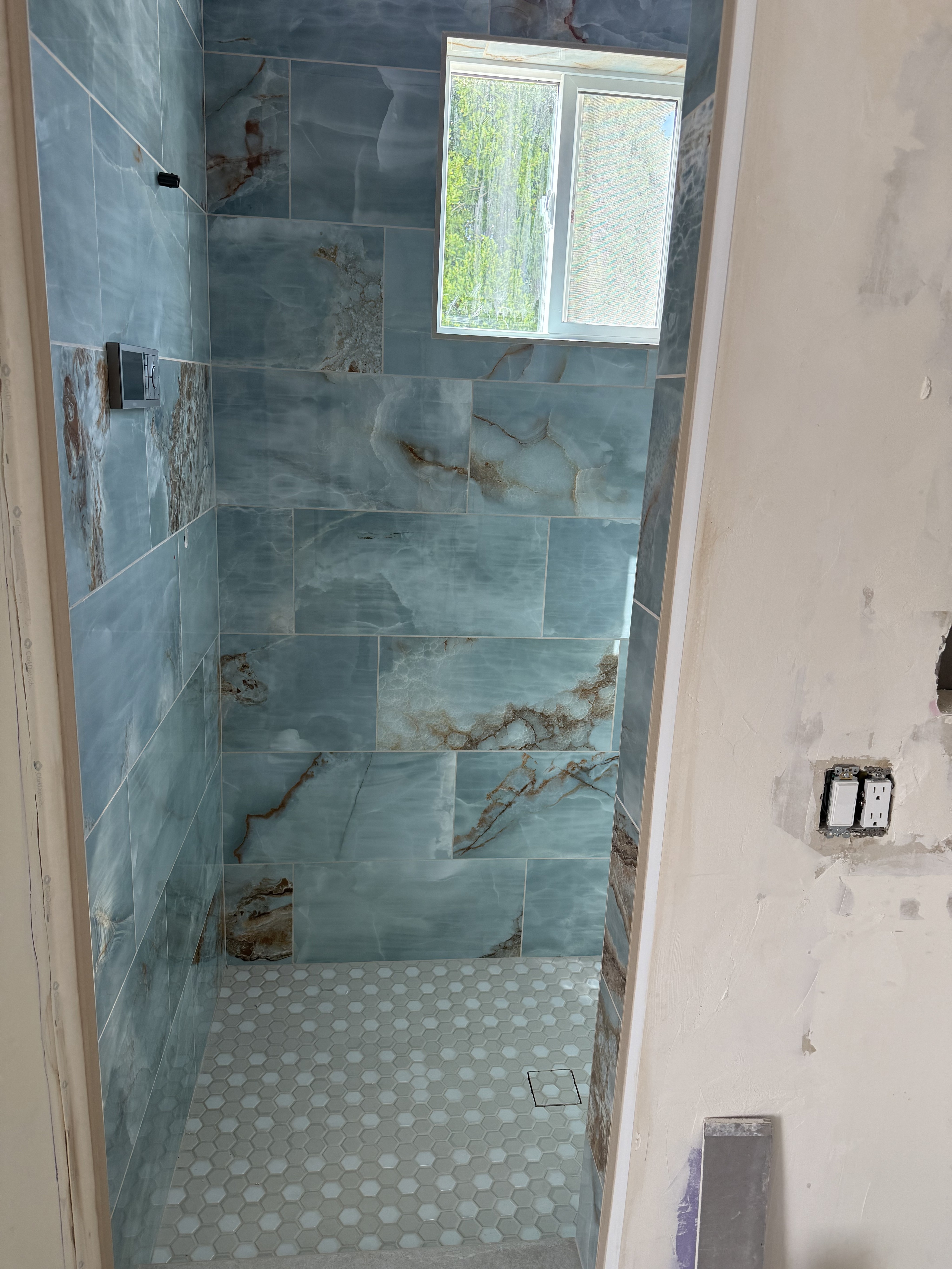 Luxurious bathroom vanity area with a dramatic wall featuring large format natural stone tiles in varying earthy tones and complex veining, serving as a striking backsplash above a double sink vanity.